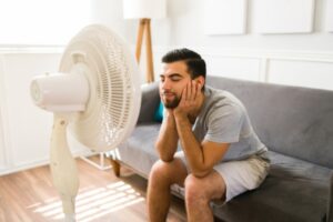man feeling relieved in front of stand fan due to excess humidity at home